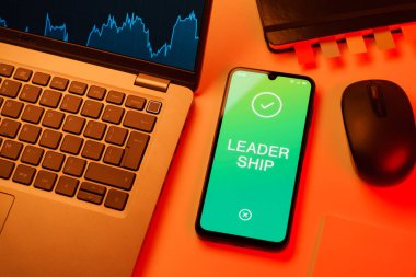 Ofis masası dizüstü bilgisayarlı ve telefonlu Liderlik metnini gösteriyor. Liderlik bir takıma rehberlik etme ve onlara ilham verme yeteneğidir..