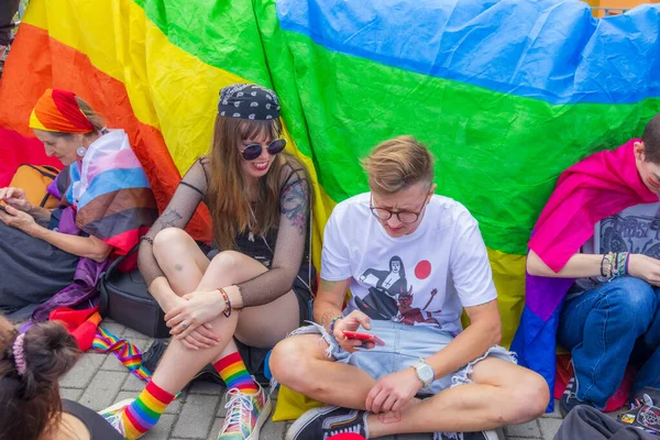 Slubice. Polonya. 13 Eylül 2025. Gurur etkinliği sırasında gökkuşağı bayrağının önünde oturan gençler renkli kıyafetler giyip çeşitliliği kutluyorlar..