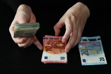 Eller siyah arka plandaki Avrupa banknotlarını sıralıyor ve sayıyor. Kağıt para biriminin 10 ve 20 banknotluk yakın çekimi. Maliye, bütçe, para denetimi ve gelir kavramı.