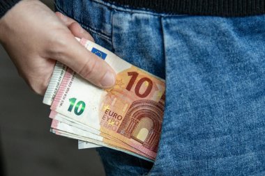 Kotun cebine yüklü miktarda Avro banknotu koyan bir elin yakın çekimi. Günlük hayatta nakit, tasarruf, maaş, bütçe ve kişisel finans kavramı.