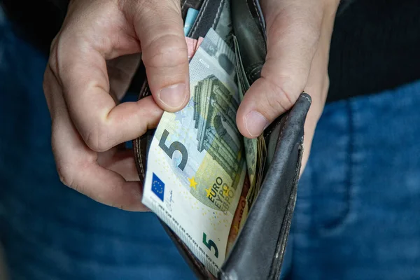 Deri bir cüzdana 5 avroluk banknot koyan ellerin yakın çekimi. Günlük yaşamda finans, harcama, nakit işleme, gelir ve kişisel bütçe kavramı.