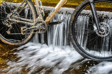 Dirty Mountain Bike Stands in a Creek Against the Small Waterfall. Dirty Chain Drive Mountain Bike close-up. Cleaning a Bicycle Concept clipart