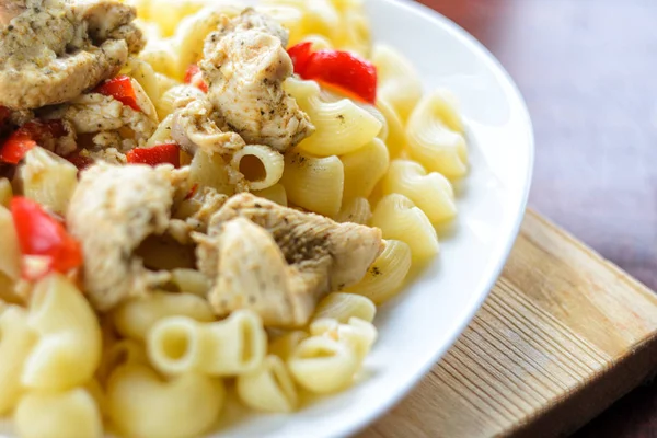 Sıcak makarna tavuk göğsü et ve sebze ahşap masa, yakın çekim üzerinde büyük beyaz plaka ile. Gıda arka plan