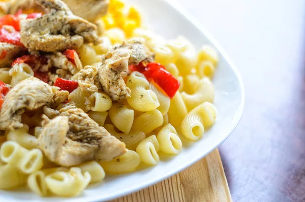 Sıcak makarna tavuk göğsü et ve sebze ahşap masa, yakın çekim üzerinde büyük beyaz plaka ile. Gıda arka plan