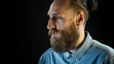 Siyah zemin üzerine mavi kot gömlekli sakallı adam portresi.