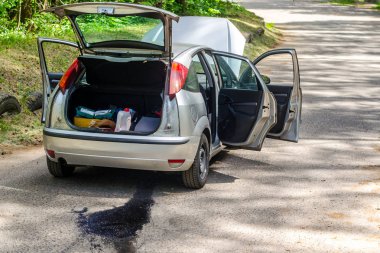Yol kenarında açık bir başlık, gövde ve kapıları ile kırık araba. Petrol sızıntısı motoru asfalt üzerinde