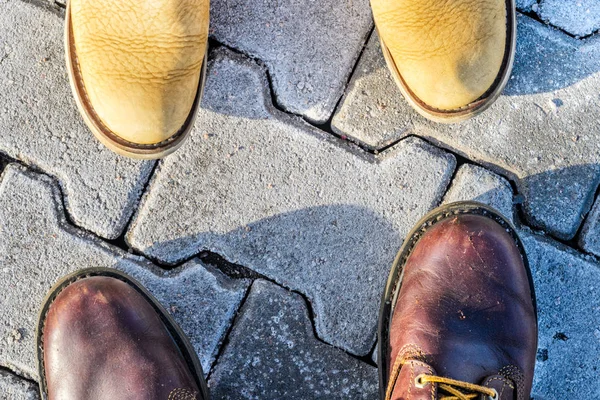 第一人称的鞋的看法 夫妇在冬天步行概念 从上面看两对黄色和棕色靴子在鹅卵石路面背景 — 图库照片