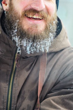 İçinde buz sarkıtları sakallı. Kahverengi spor ceketli gülümseyen bir genç adamın yüzünü parçası. Kış sporları açık havada kavramı.