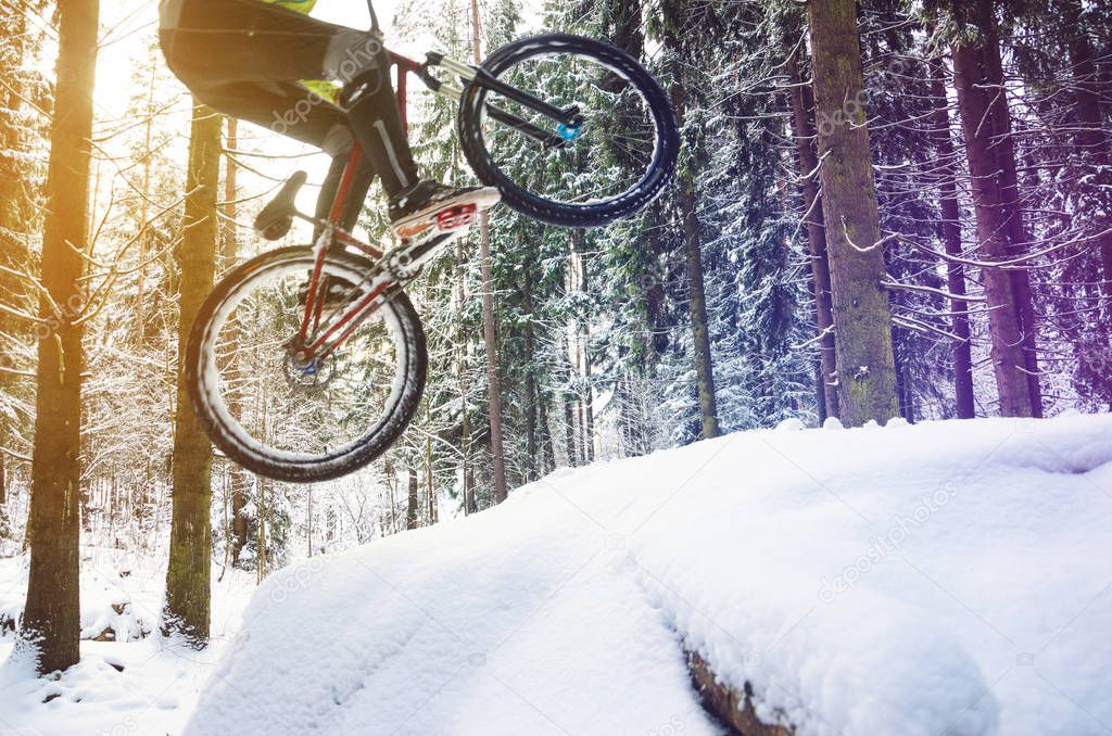 Silhouette of a cyclist in a jump. Mountain biking on trails in a snowy forest. Extreme winter sport. Bike rider flies through the air