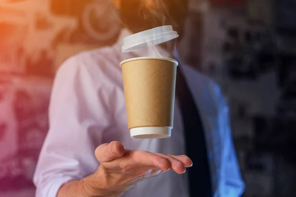 Barista in a white shirt with a tie holds floating in the air a paper cup with a hot drink on his outstretched arms. Barista wizard concept. Background for advertising and placing logo on your drink