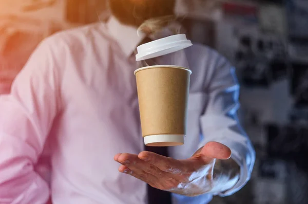 Barista in a white shirt with a tie holds floating in the air a paper cup with a hot drink on his outstretched arms. Barista wizard concept. Background for advertising and placing logo on your drink