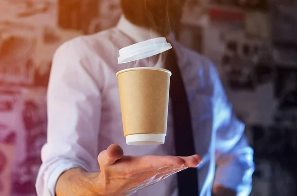 Barista in a white shirt with a tie holds floating in the air a paper cup with a hot drink on his outstretched arms. Barista wizard concept. Background for advertising and placing logo on your drink