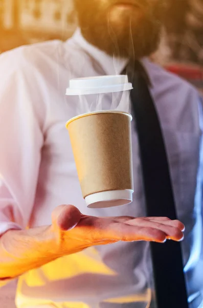 Barista in a white shirt with a tie holds floating in the air a paper cup with a hot drink on his outstretched arms. Barista wizard concept. Background for advertising and placing logo on your drink