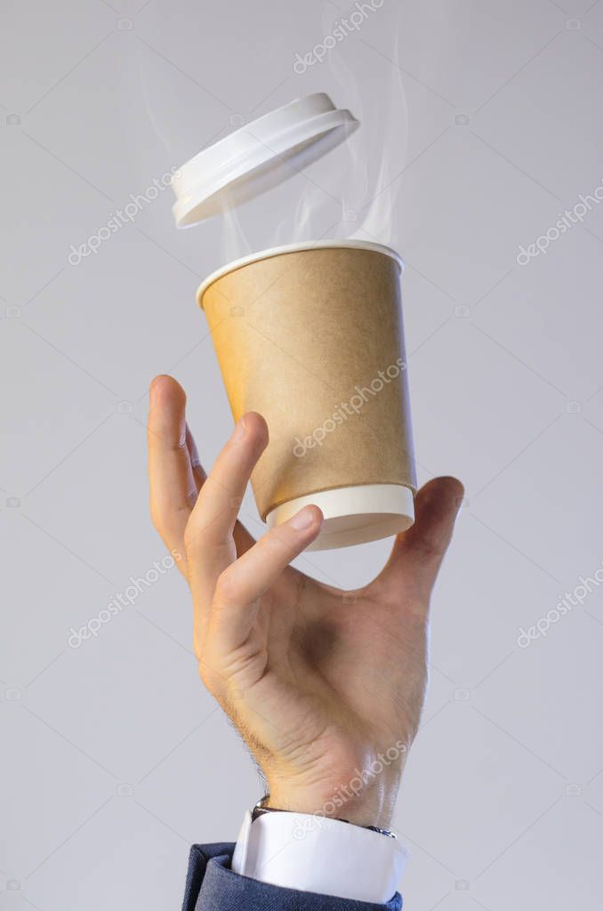 Hand of a business man in a blue jacket, white shirt and watch catches a flying cup of hot coffee with steam from a drink. Coffee break advertising concept. Empty place for your logo placement.