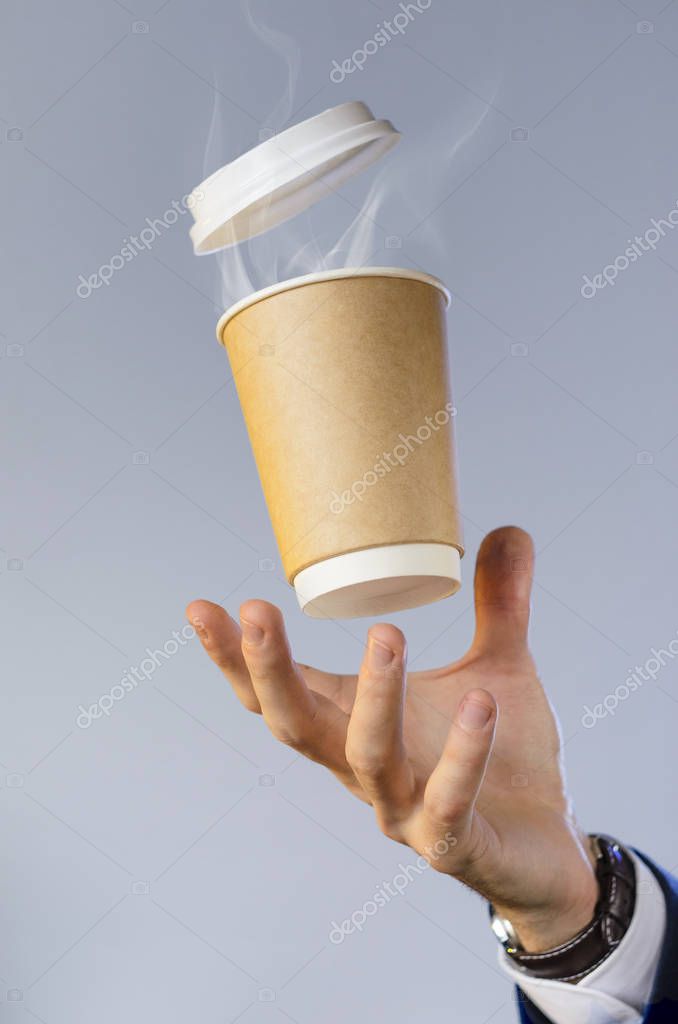 Hand of a business man in a blue jacket, white shirt and watch catches a flying cup of hot coffee with steam from a drink. Coffee break advertising concept. Empty place for your logo placement.