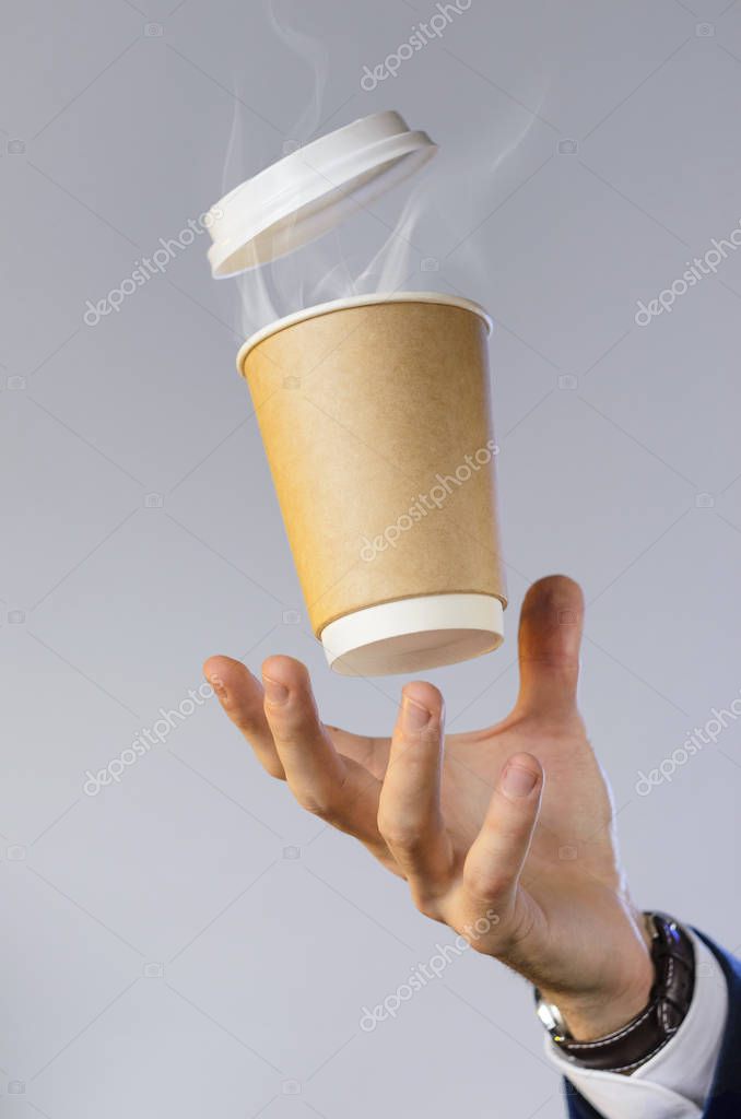 Hand of a business man in a blue jacket, white shirt and watch catches a flying cup of hot coffee with steam from a drink. Coffee break advertising concept. Empty place for your logo placement.