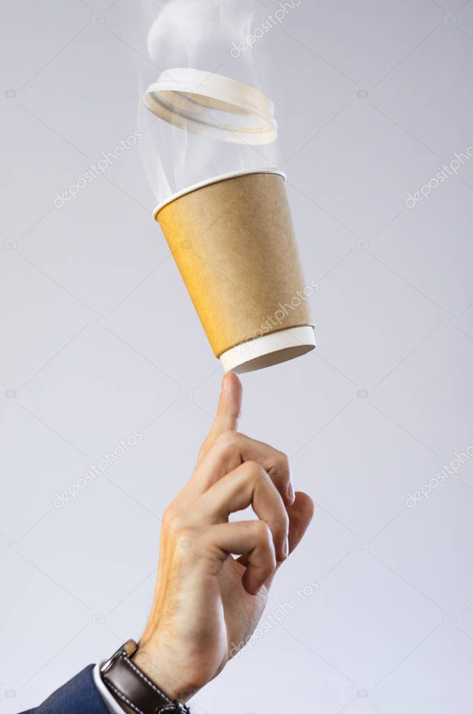 Hand of a Business Man in a Jacket, Shirt and Watch Balances Paper Cup of Hot Coffee on a Fingertip. Levitating Plastic Cup Lid. Coffee Break Concept. Empty Place for Your Logo. Layout for Advertising