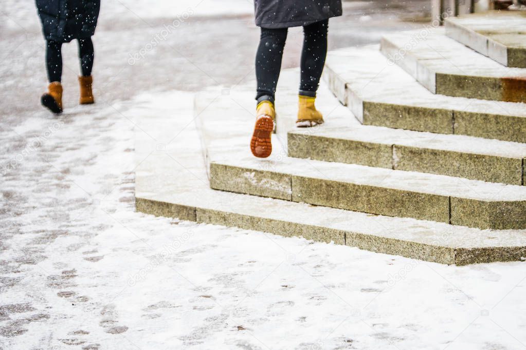 Winter Walk in Yellow Leather Boots. Back view on the feet of a women rises on icy snowy granite steps in urban environment. Abstract empty blank winter weather background