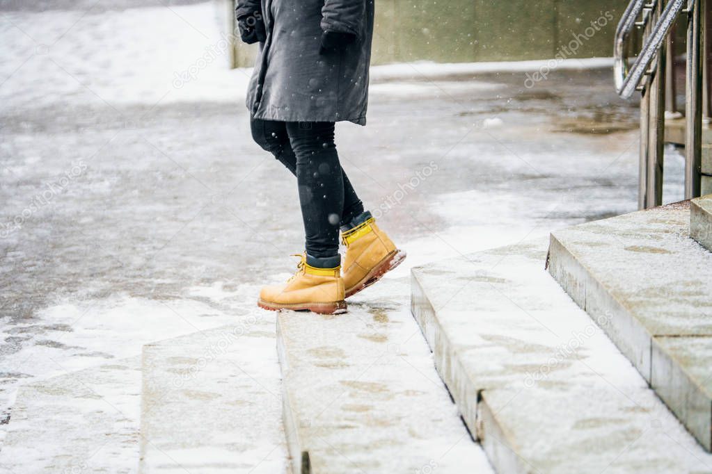 Winter Walk in Yellow Leather Boots. Back view on the feet of a women rises on icy snowy granite steps in urban environment. Abstract empty blank winter weather background