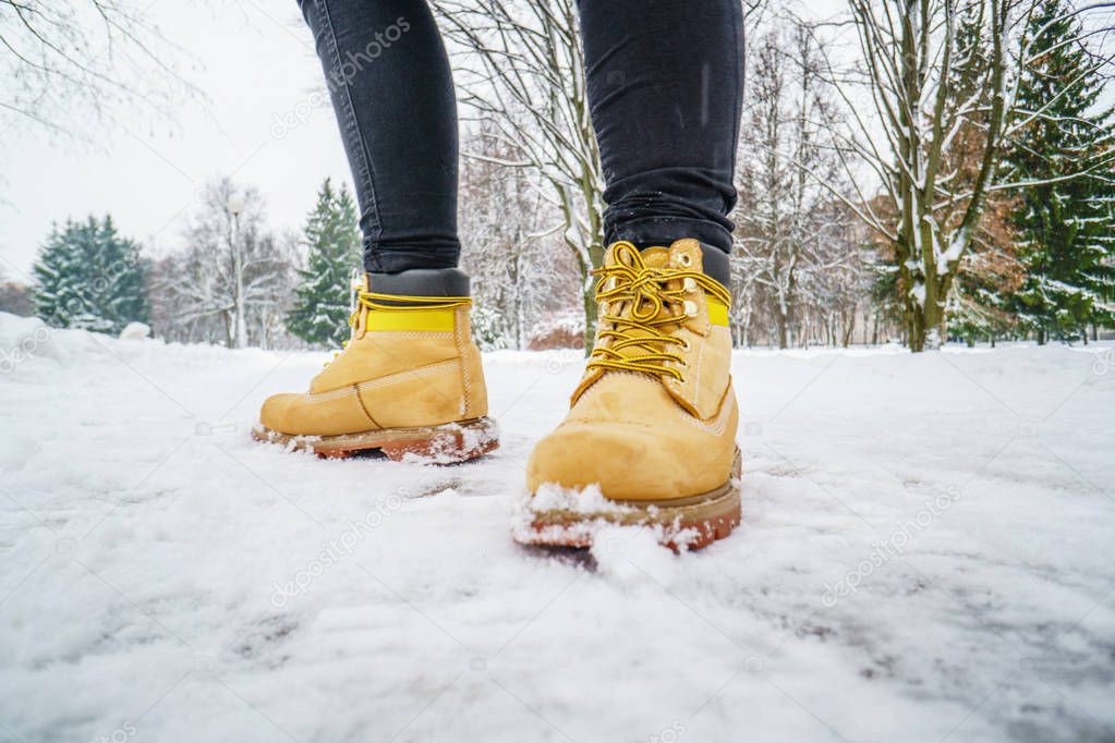 Winter Walk in Yellow Leather Boots. Front view on the feet of a man walking along the icy snowy pavement. Pair of shoe on icy road in winter. Abstract empty blank winter weather background