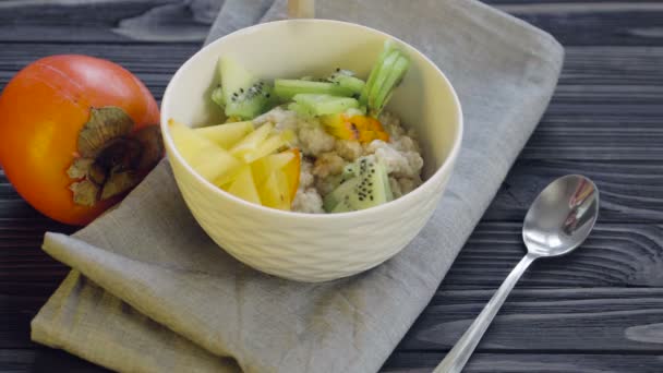 健康食品 深いボウルビューで柿とキウイとオートミール 健康的な朝食を調理する クルミを追加 — ストック動画