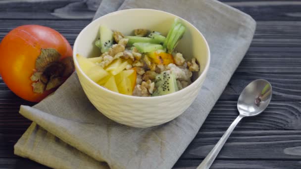 健康食品 深いボウルビューで柿とキウイとオートミール 健康的な朝食を調理する クルミを追加 — ストック動画