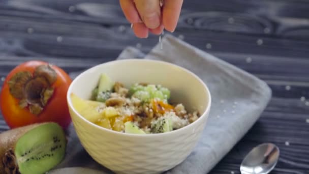 Une nourriture saine. Farine d'avoine au kaki, kiwi et noix dans un bol profond vue sur le dessus. Cuisson saine petit déjeuner - main féminine ajoutant des graines de sésame 