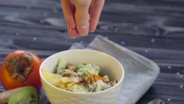 Une nourriture saine. Farine d'avoine au kaki, kiwi et noix dans un bol profond vue sur le dessus. Cuisson saine petit déjeuner - main féminine ajoutant des graines de sésame 