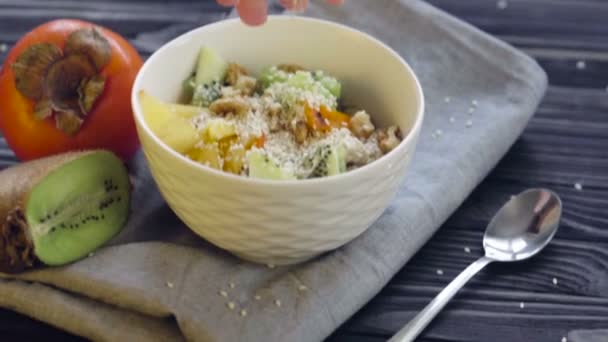 Une nourriture saine. Farine d'avoine au kaki, kiwi et noix dans un bol profond vue sur le dessus. Cuisson saine petit déjeuner - main féminine ajoutant des graines de sésame 