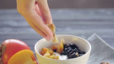 Sağlıklı yiyecekler. Derin bir kasede yulaf ezmesi. Sağlıklı kahvaltı hazırlıyorum. Kadın eli kuru erikli yulaf ezmesine kayısı ekliyor.