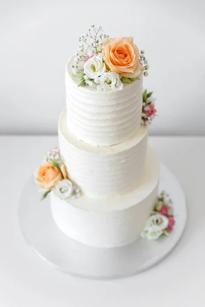 Wedding cake with three tiers with natural flowers on a white table