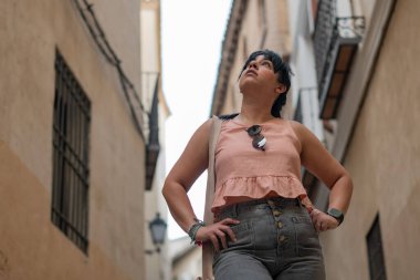 Dar bir Avrupa geçidinde duran kadın, elleri kalçasında, etrafındaki mimariye bakıyor.