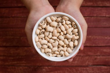 Beyaz kasede siyah gözlü fasulye tutan eller.