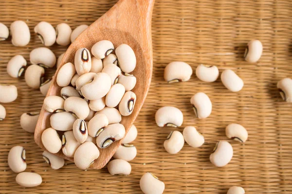 Black-eyed beans in wooden spoon on a reed mat.