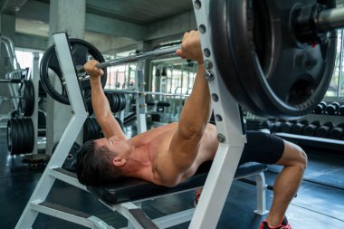 Spor salonunda spor yapmak için halter plakalı kaslı bir adam çalışıyor..