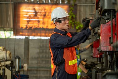 Makine dairesinde güvenlik şapkası takan Asyalı bir işçi fabrikada makineyle çalışıyor..