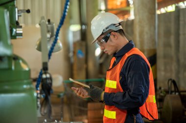 Fabrikada makineyle çalışan Asyalı bir işçi cep telefonunda uygulamayı kullanıyor..