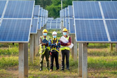 Güneş enerjisi santralinde çalışan ve kontrol eden sağlık maskesi takan bir mühendis, güneş enerjisi panelleri, yenilenebilir enerji dostu yönetim sistemleri kavramı.