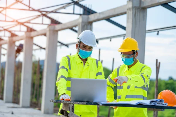 Two engineers wearing protective mask to Protect Against Covid-19 and checking production process in building construction site,Construction,Building, teamwork and people concept.