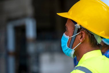 Covid-19 'a karşı korunmak için koruyucu maske takan ve inşaat alanında üretim sürecini kontrol eden mühendis Mühendis, İnşaat, Coronavirus küresel bir acil durum haline geldi..
