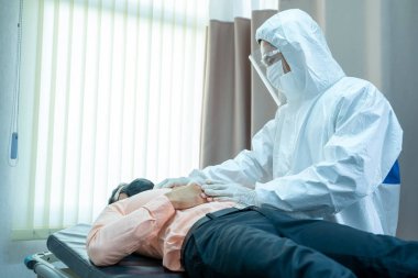 Tehlikeli madde koruma giysisi giyen doktor muayene odasında hastayı rahatlatan plastik eldivenler giyiyor..