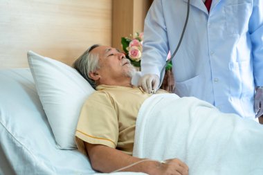 Revirdeki tıbbi ekip, hastanedeki yaşlı erkek hastanın yatağının etrafında toplanıyor, doktorlar raporları pano üzerinde tartışıyor..