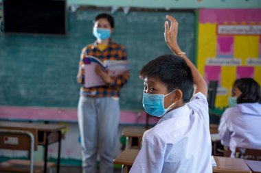 Covid-19 'a karşı korunmak için koruyucu maske takan bir grup Asyalı ilkokul öğrencisi, öğretmeniyle aynı sınıfta okuyan üniformalı öğrenciler, okullarını tekrar açarlar..