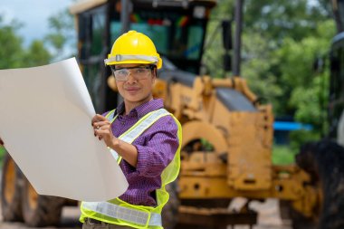 İnşaat alanında yükleyici kamyonla planları tutan mühendis ya da mimar kadınlar, iş alanında inşaat otomobili..