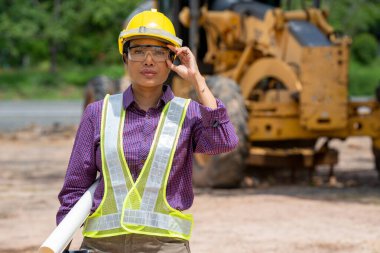 İnşaat alanında buldozer kamyonuyla duran sarı kasklı kadın inşaat mühendisi ya da mimar..