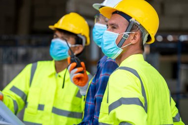 İnşaat alanındaki teftiş sırasında koruyucu yüz maskesi takan grup inşaat mühendisi Coronavirus küresel bir acil durum haline geldi..