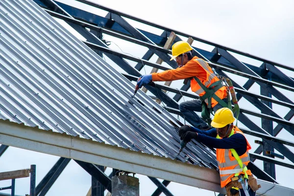 İnşaat işçisi inşaat sahasına yeni çatı döşedi. Metal levhalı yeni çatılarda kullanılan elektrikli matkap..