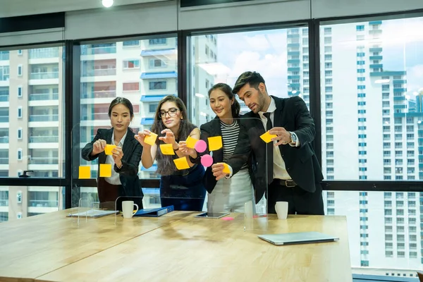 Group of diversity people searching information for provide ideas in new startup project and standing behind glass wall with sticky colorful papers.Cheerful students learning words from stickers.