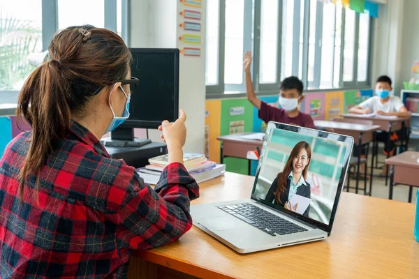 Teacher  wearing protective mask to Protect Against Covid-19 is teaching school kids sitting in classroom online ,Elementary school,Learning and people concept.