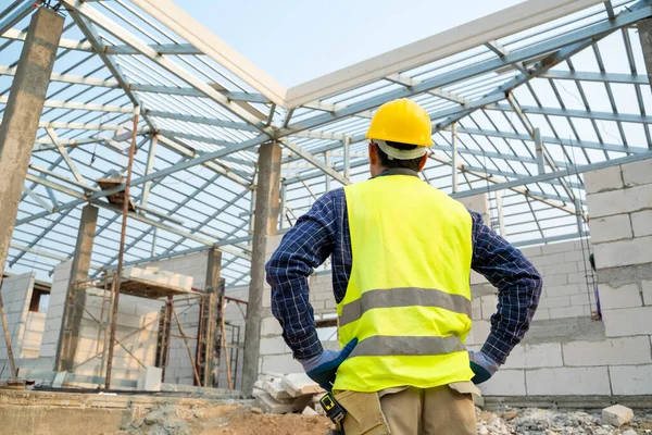 Construction engineer wearing safety vest and yellow helmet working at house building site,House construction concept.